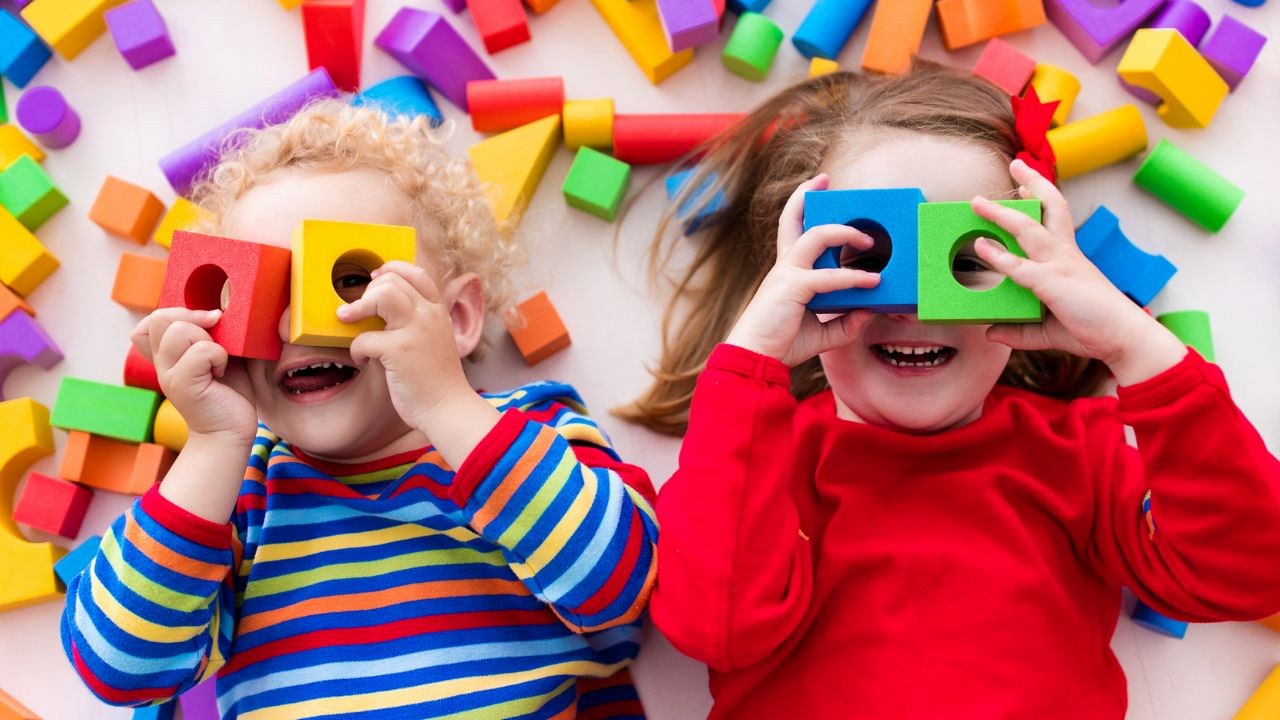 Smiling preschoolers laying on wooden blocks and holding blocks up to their face.